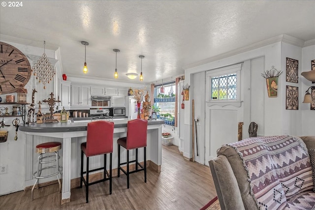 kitchen with pendant lighting, light hardwood / wood-style floors, a kitchen bar, a textured ceiling, and white cabinets