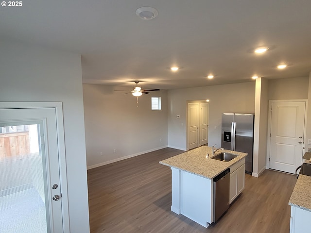 kitchen featuring a kitchen island with sink, stainless steel appliances, wood finished floors, a sink, and baseboards