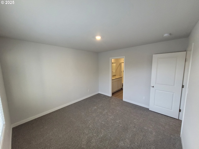 unfurnished bedroom with baseboards, dark colored carpet, and connected bathroom