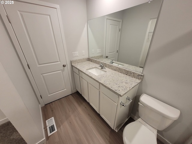 half bath with toilet, wood finished floors, vanity, and visible vents