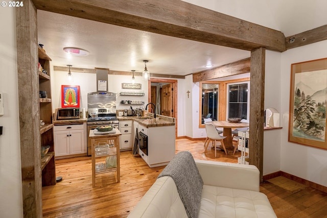 kitchen with wall chimney exhaust hood, stainless steel appliances, sink, light wood-type flooring, and white cabinetry