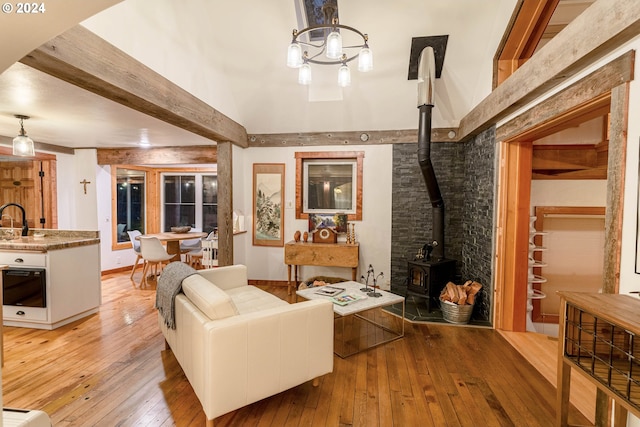 living room with beam ceiling, sink, light wood-type flooring, and a wood stove