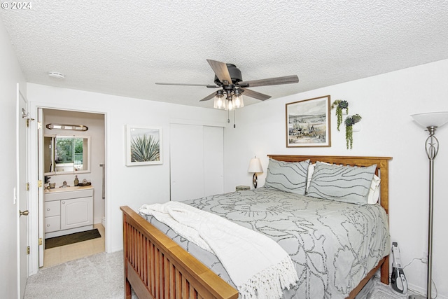 carpeted bedroom with a closet, ensuite bath, a textured ceiling, and ceiling fan