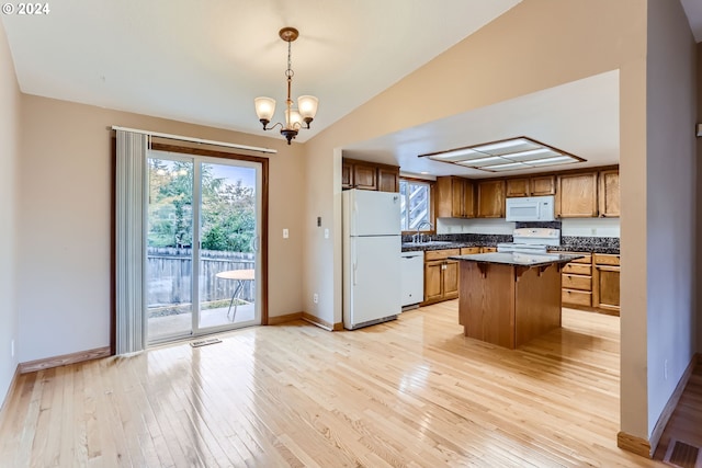 kitchen featuring a center island, lofted ceiling, white appliances, hanging light fixtures, and a kitchen bar