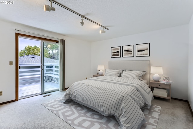 carpeted bedroom with a textured ceiling, rail lighting, and access to outside