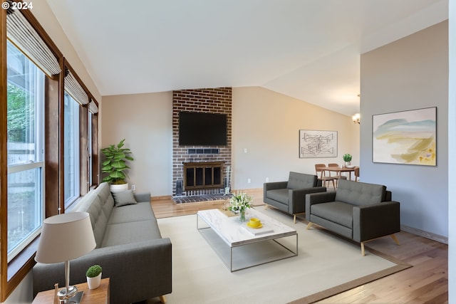 living room featuring plenty of natural light, light hardwood / wood-style flooring, lofted ceiling, and a brick fireplace