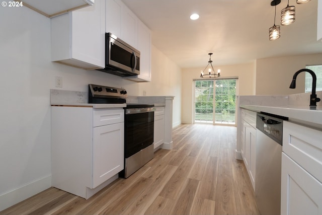 kitchen featuring white cabinets, pendant lighting, a chandelier, appliances with stainless steel finishes, and light wood-type flooring