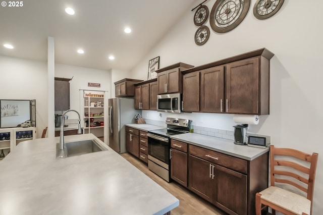 kitchen with vaulted ceiling, appliances with stainless steel finishes, sink, dark brown cabinetry, and light hardwood / wood-style flooring