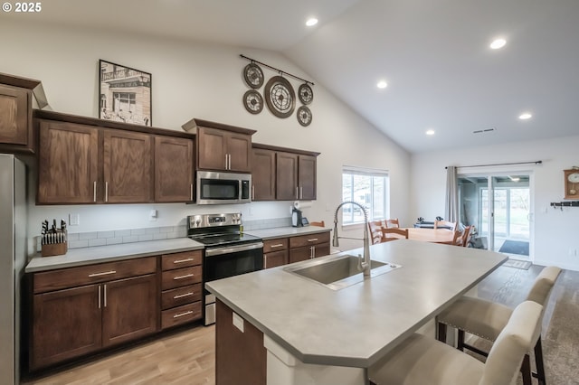 kitchen featuring a kitchen bar, sink, a center island with sink, light hardwood / wood-style flooring, and appliances with stainless steel finishes