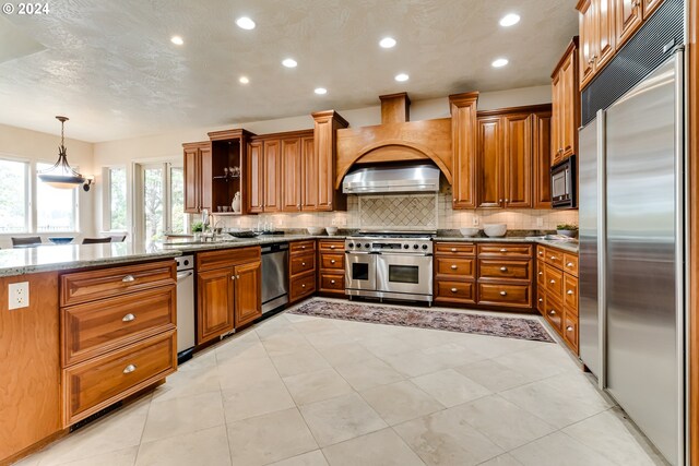 kitchen with decorative backsplash, built in fridge, sink, light stone countertops, and kitchen peninsula