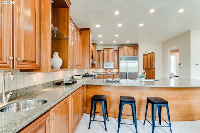 kitchen with built in refrigerator, white microwave, a kitchen breakfast bar, and a sink