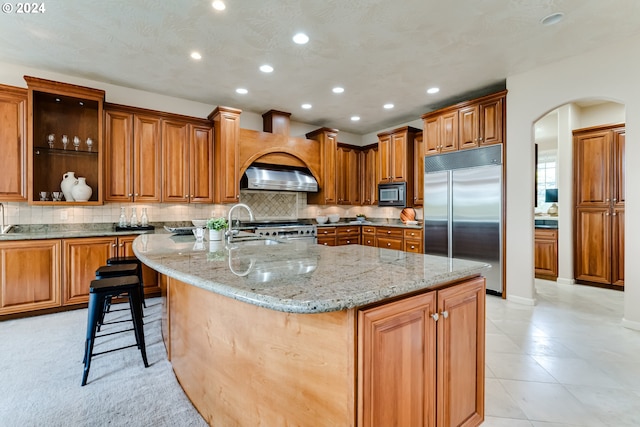 kitchen featuring arched walkways, decorative backsplash, built in appliances, light stone countertops, and a sink