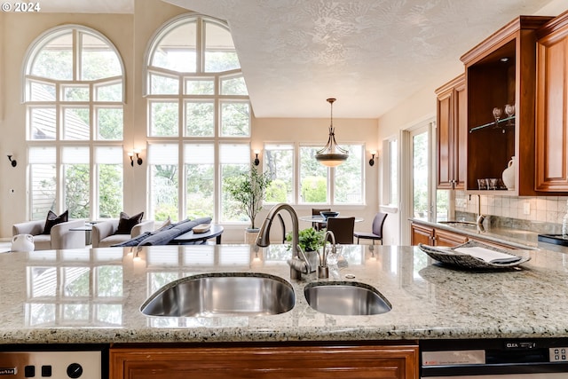 kitchen featuring brown cabinets, a sink, a textured ceiling, light stone countertops, and dishwasher