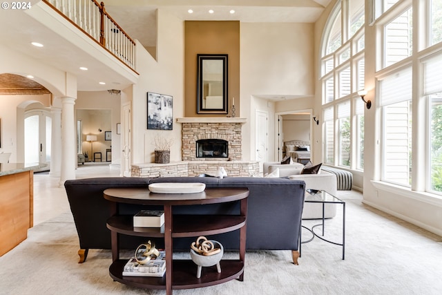 living room featuring light colored carpet, a high ceiling, a fireplace, baseboards, and decorative columns