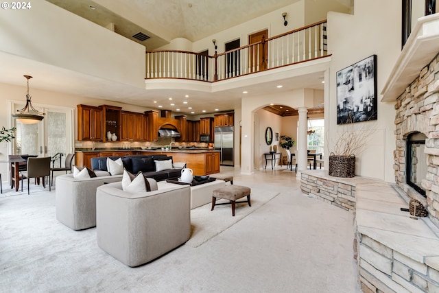 living room featuring arched walkways, visible vents, a towering ceiling, a stone fireplace, and ornate columns