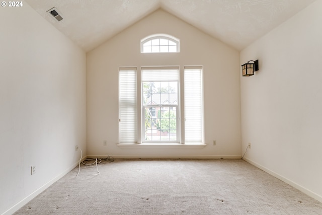 carpeted empty room with visible vents, vaulted ceiling, and baseboards