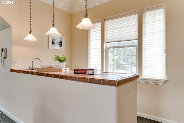 kitchen with a peninsula, a sink, baseboards, hanging light fixtures, and tile counters