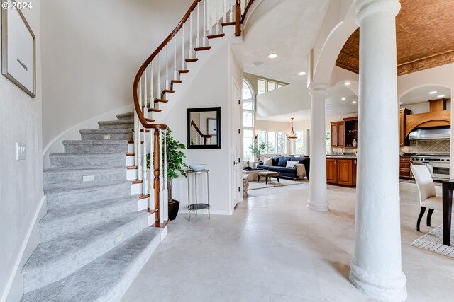 sitting room featuring high vaulted ceiling, light tile patterned flooring, and decorative columns