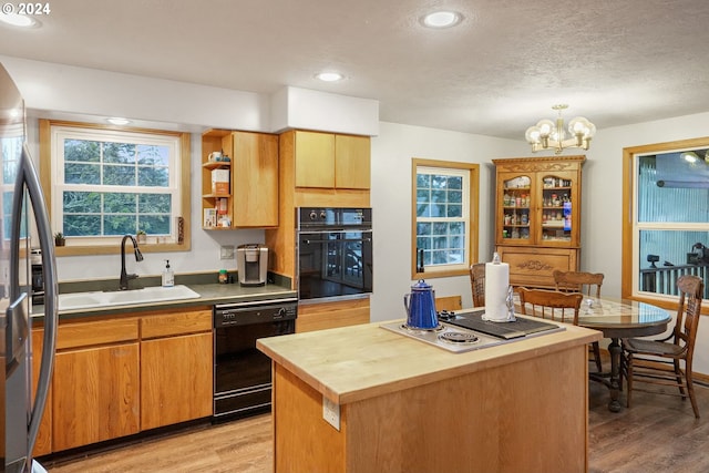 kitchen with light wood-type flooring, sink, black appliances, a chandelier, and a center island