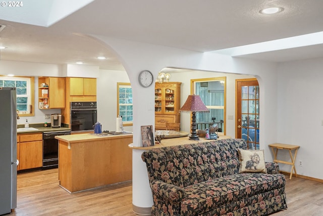 kitchen featuring black appliances, plenty of natural light, a kitchen island, and light wood-type flooring