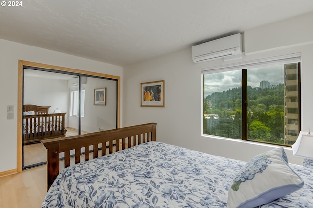 bedroom with an AC wall unit, multiple windows, a closet, and light hardwood / wood-style flooring