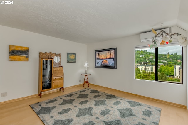 unfurnished room featuring hardwood / wood-style floors, a textured ceiling, vaulted ceiling, and a wall mounted AC