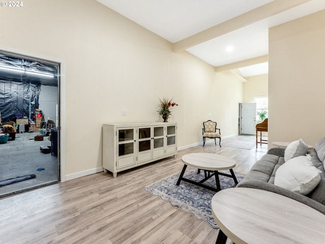 living area featuring light wood-style floors, vaulted ceiling with beams, and baseboards