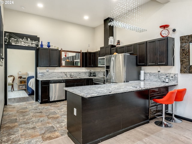 kitchen featuring baseboards, appliances with stainless steel finishes, a peninsula, light stone countertops, and a high ceiling