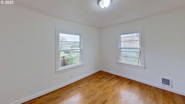 empty room with baseboards, visible vents, and hardwood / wood-style flooring