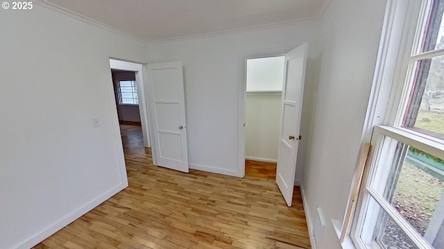 unfurnished bedroom featuring light wood-style flooring, a walk in closet, crown molding, and baseboards