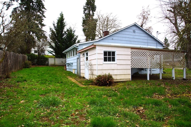 rear view of property featuring a chimney, fence, and a lawn