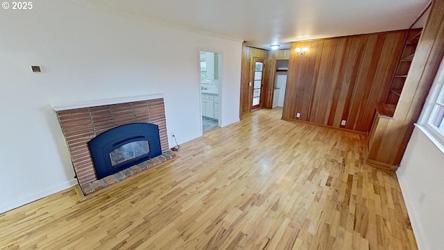 unfurnished living room featuring wooden walls, light hardwood / wood-style flooring, ornamental molding, and a brick fireplace