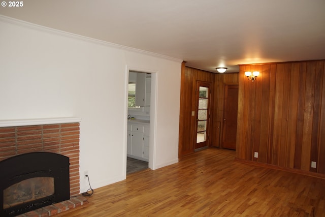 unfurnished living room with crown molding, wooden walls, wood finished floors, a brick fireplace, and baseboards