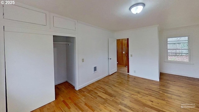 unfurnished bedroom featuring ornamental molding, a closet, light wood finished floors, and visible vents