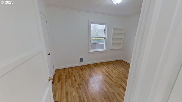 empty room with visible vents, crown molding, light wood-style floors, and baseboards