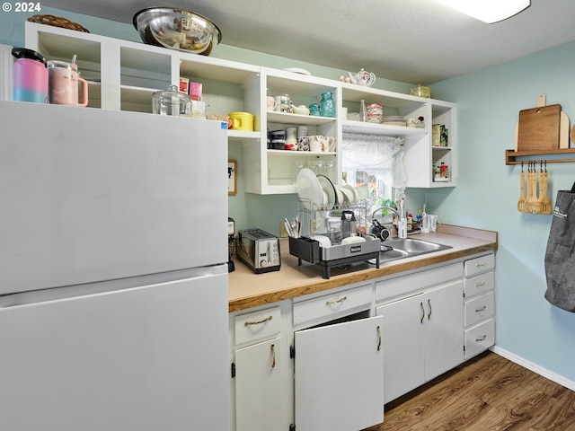 kitchen with sink, white cabinetry, white fridge, and hardwood / wood-style flooring