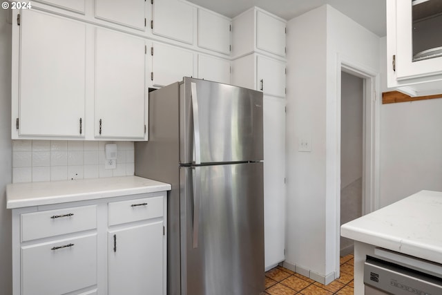 kitchen featuring stainless steel fridge, white cabinets, light tile patterned floors, and backsplash