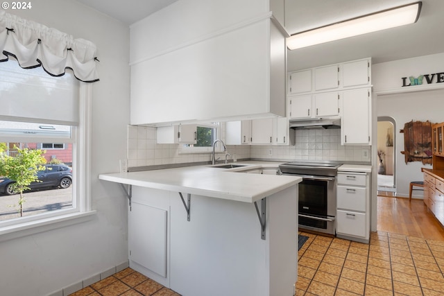 2405 Maple St, Longview, WA 98632 - kitchen featuring stainless steel electric range oven, a sink, a peninsula, under cabinet range hood, and white cabinetry