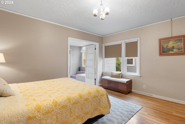 bedroom with a textured ceiling, wood-type flooring, connected bathroom, ornamental molding, and a notable chandelier