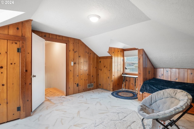 bedroom with lofted ceiling, a textured ceiling, and wooden walls