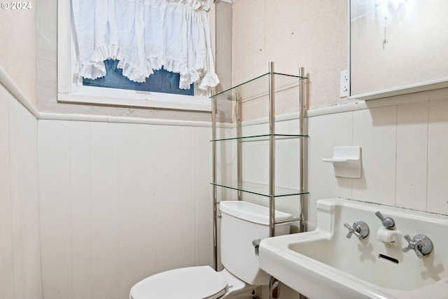 bathroom featuring toilet, wood walls, and sink