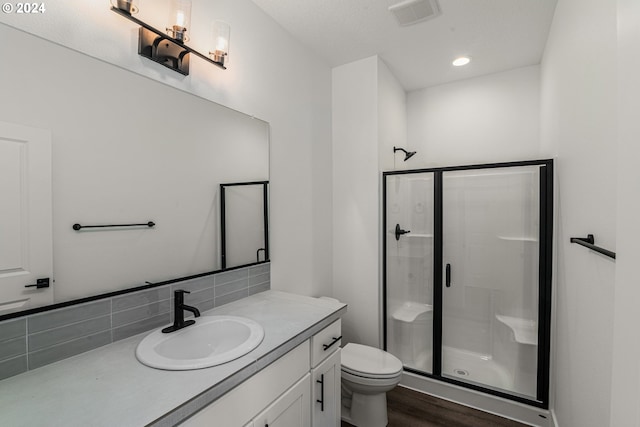 bathroom featuring toilet, a shower with shower door, backsplash, wood-type flooring, and vanity