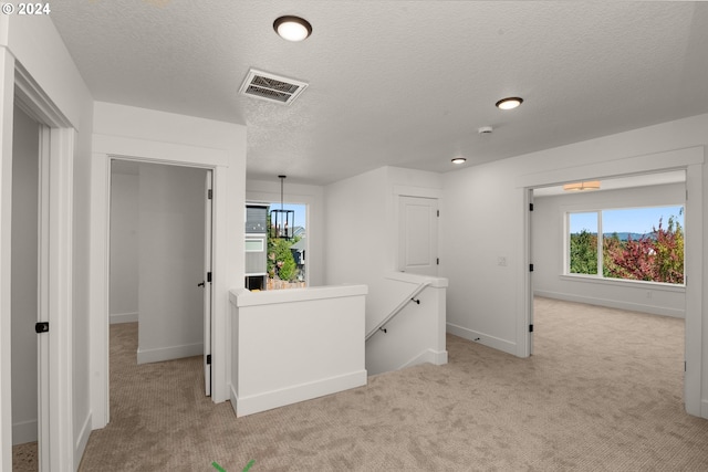 hall featuring a textured ceiling, an inviting chandelier, and light colored carpet