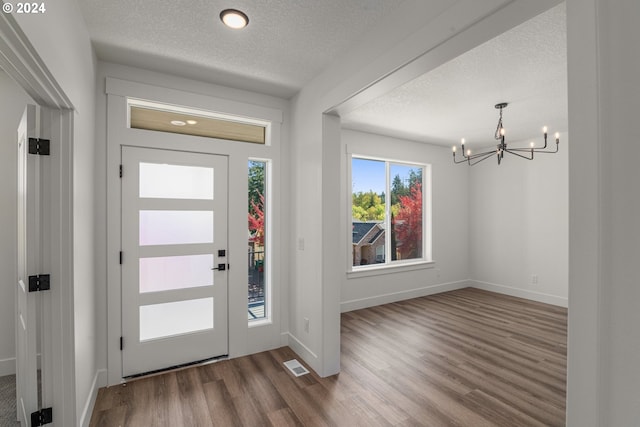 entryway with a textured ceiling, a wealth of natural light, a chandelier, and hardwood / wood-style floors