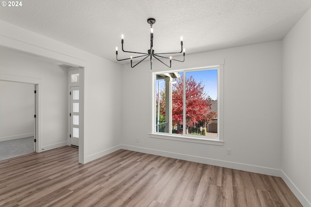 unfurnished dining area featuring an inviting chandelier, a textured ceiling, and light hardwood / wood-style floors