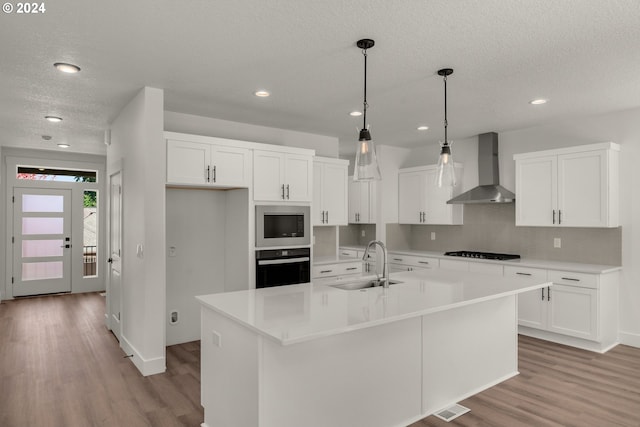 kitchen with a center island with sink, black appliances, sink, white cabinetry, and wall chimney exhaust hood