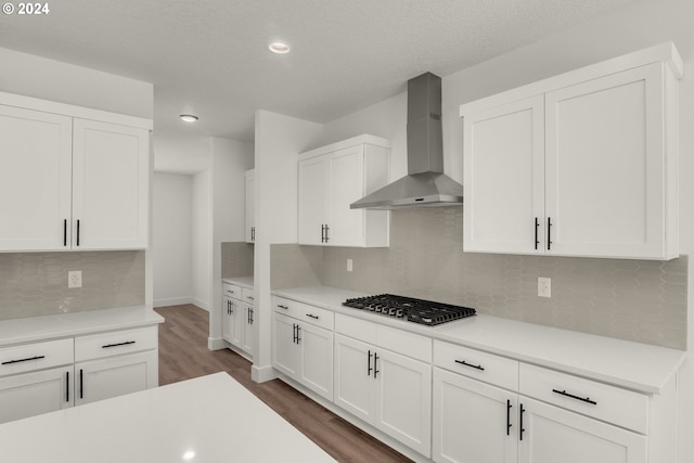 kitchen featuring dark hardwood / wood-style flooring, white cabinets, stainless steel gas stovetop, and wall chimney exhaust hood