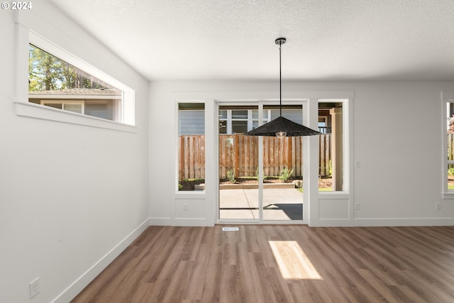 unfurnished dining area with wood-type flooring and a textured ceiling