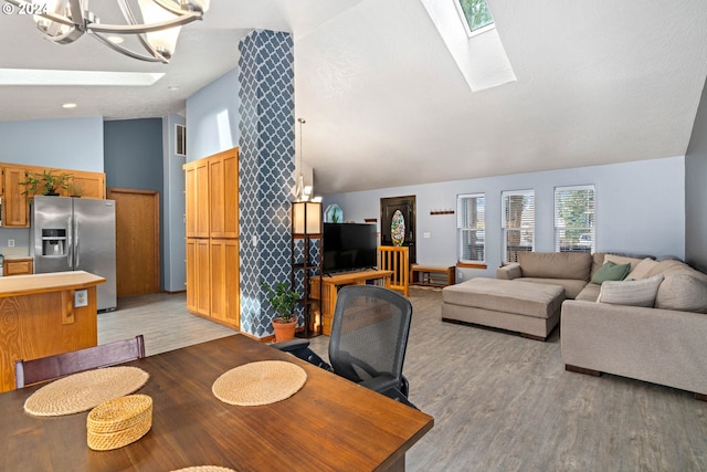 dining area with vaulted ceiling with skylight, a notable chandelier, and light wood-style flooring