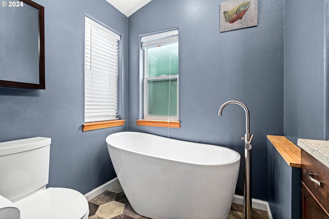 full bath with a freestanding tub, toilet, baseboards, vanity, and a textured wall